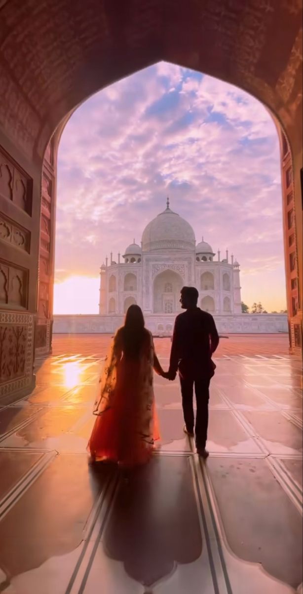 a man and woman holding hands while walking through an archway to the tajwa