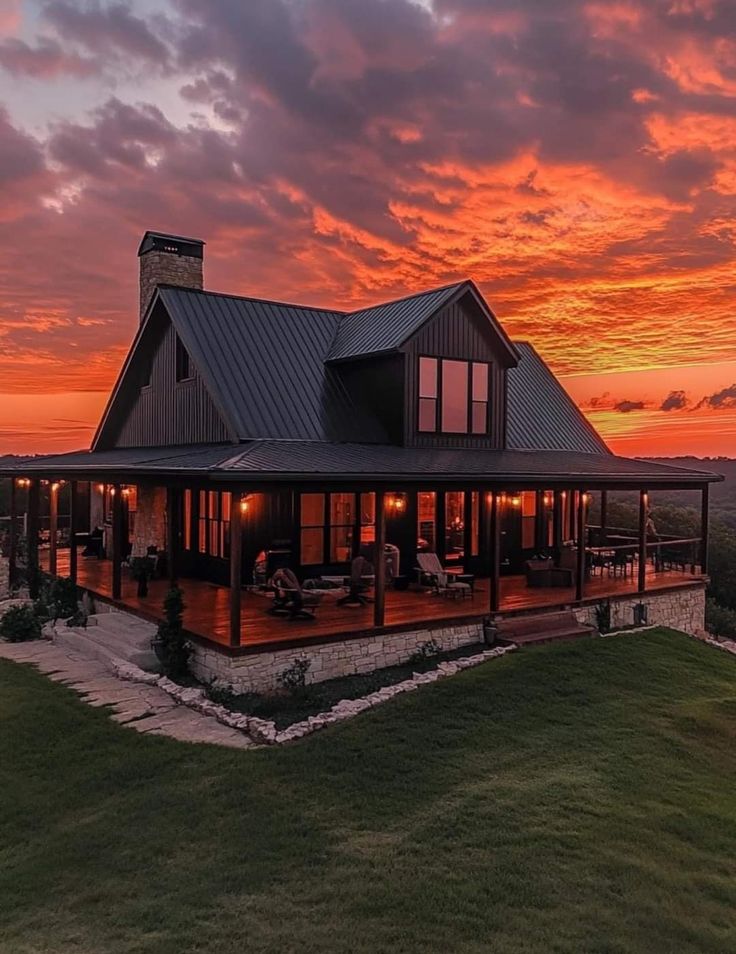 a large house sitting on top of a lush green field next to a forest at sunset