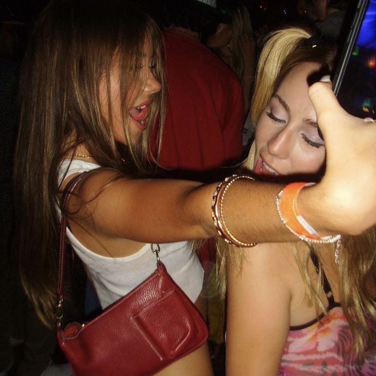 two young women taking pictures with their cell phones at a club or bar, one woman is holding her phone up to the camera