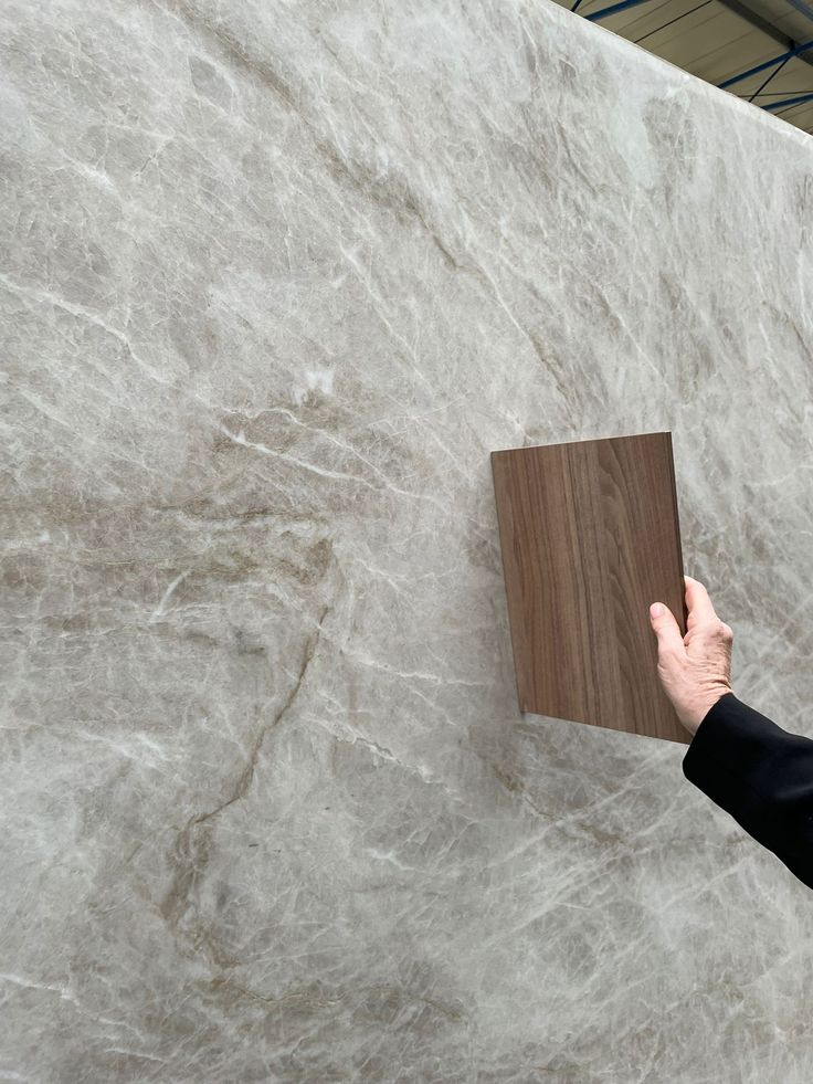 a person holding a piece of wood in front of a marble wall