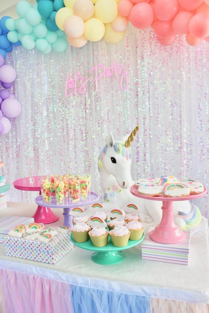 a table topped with lots of cupcakes and cake next to a unicorn statue