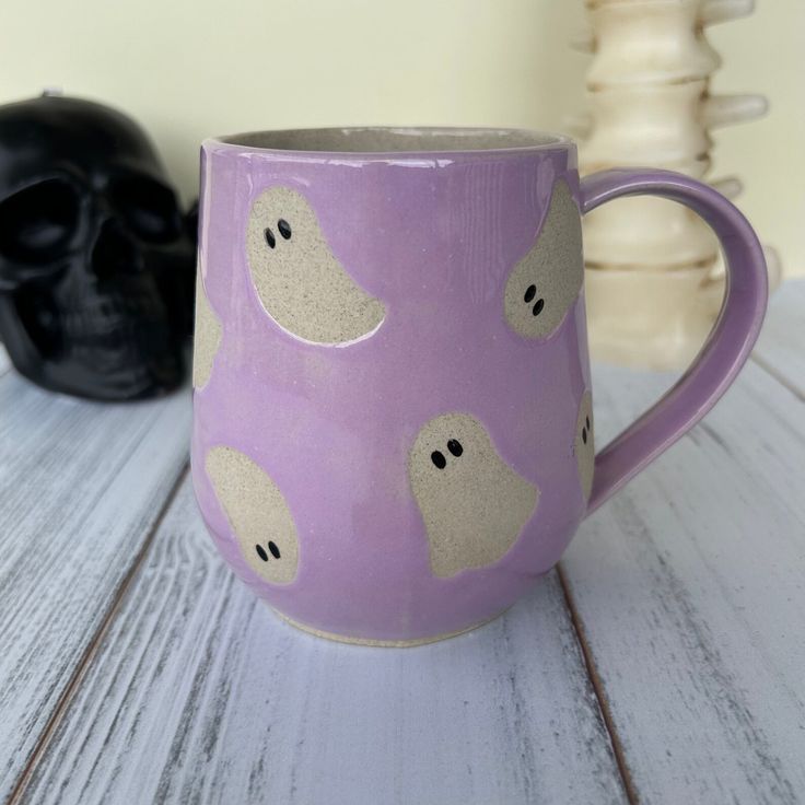 a purple coffee mug sitting on top of a wooden table next to a black skull