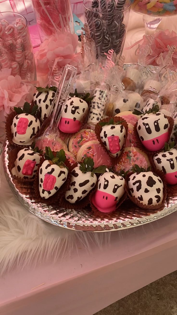 a plate full of chocolate covered strawberries with pink frosting on them and candy in the shape of cow's heads