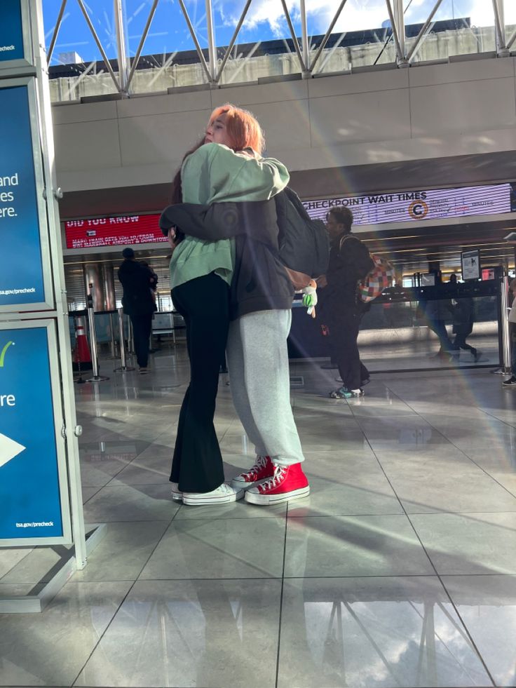 two people standing next to each other in an airport terminal with their arms around each other