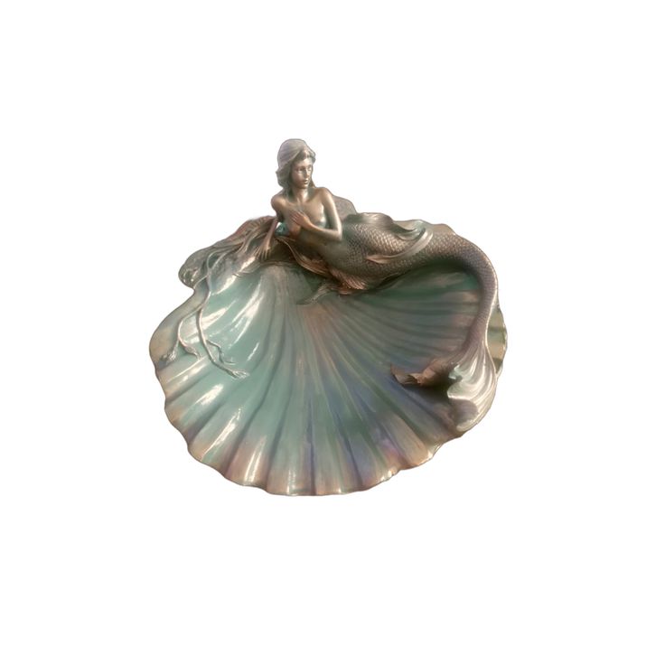 a mermaid figurine sitting on top of a green shell with a white background