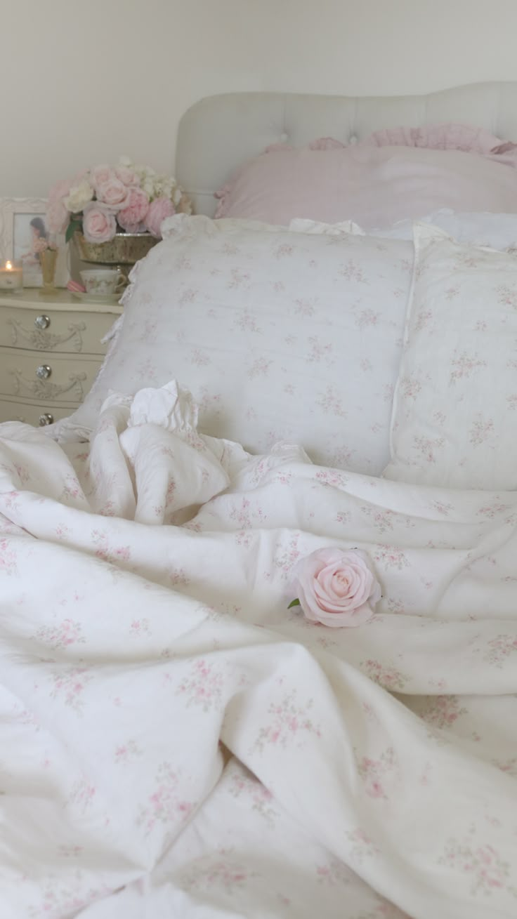 an unmade bed with white sheets and pink flowers