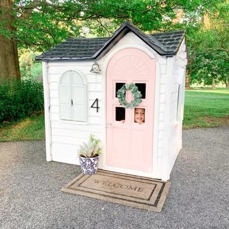 a small white house with a pink door and wreath on the front, next to a welcome mat