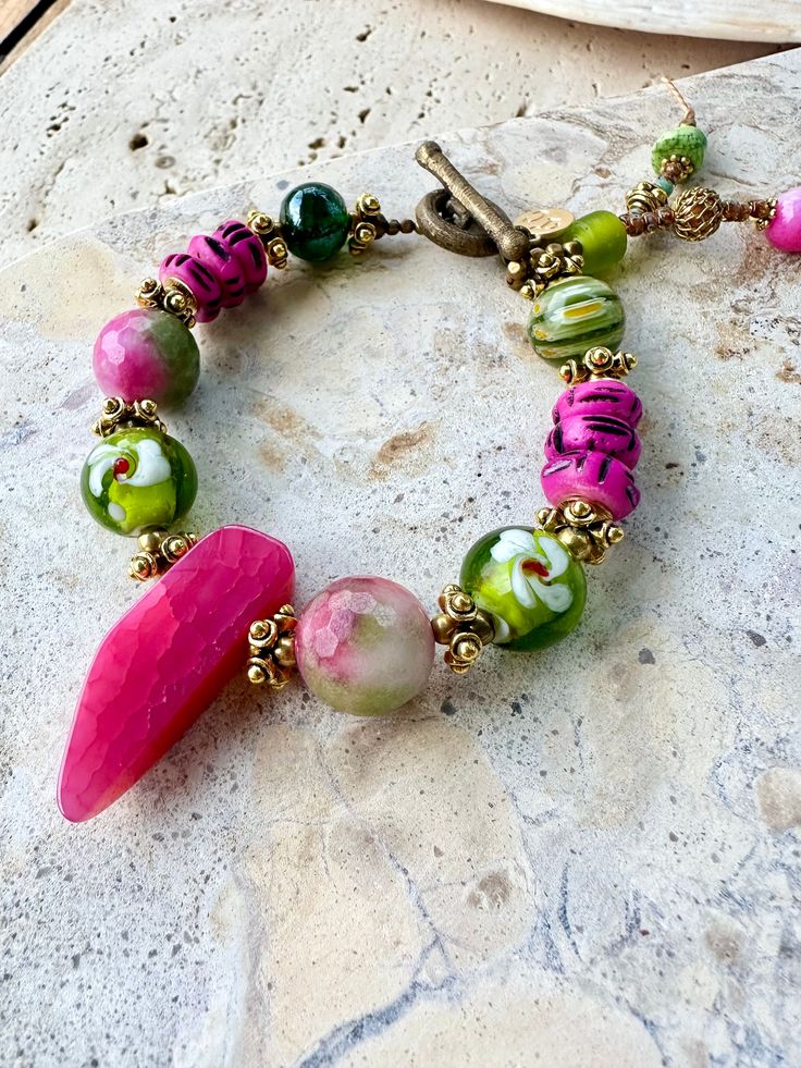 Large hot pink agate centre piece stone, set with venetian glass beads, pink-green agate stones, handprinted African hot pink bone beads, Vintage Indian gold spacer beads, finished of with a vintage African brass loop clasp. Stone and glass trinkets on the end. Pink Artisan Beaded Jewelry, Pink Beaded Czech Glass Jewelry, Pink Bohemian Jewelry With Faceted Beads, Bohemian Pink Jewelry With Faceted Beads, Handmade Pink Czech Glass Jewelry, Artisan Pink Jewelry With Round Beads, Pink Glass Jewelry With Colorful Beads, Handmade Pink Glass Jewelry, Artisan Pink Hand-strung Jewelry