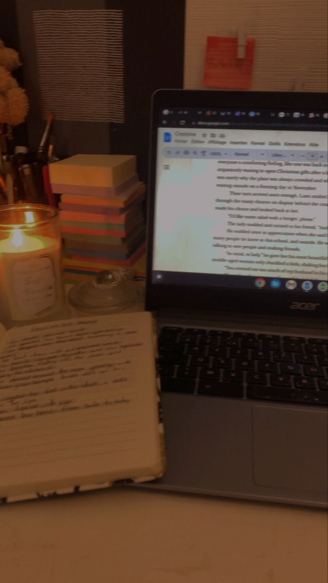 a laptop computer sitting on top of a desk next to a notebook and candlelight