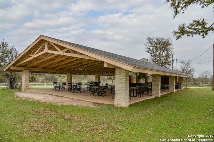 a covered picnic area in the middle of a field with tables and chairs on it