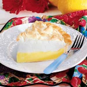 a slice of lemon pie on a plate with a fork next to it and some flowers in the background