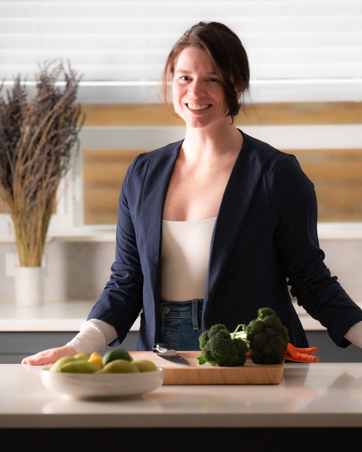 a woman standing in front of a cutting board with vegetables