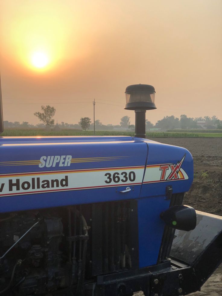 a blue tractor with the sun setting in the background