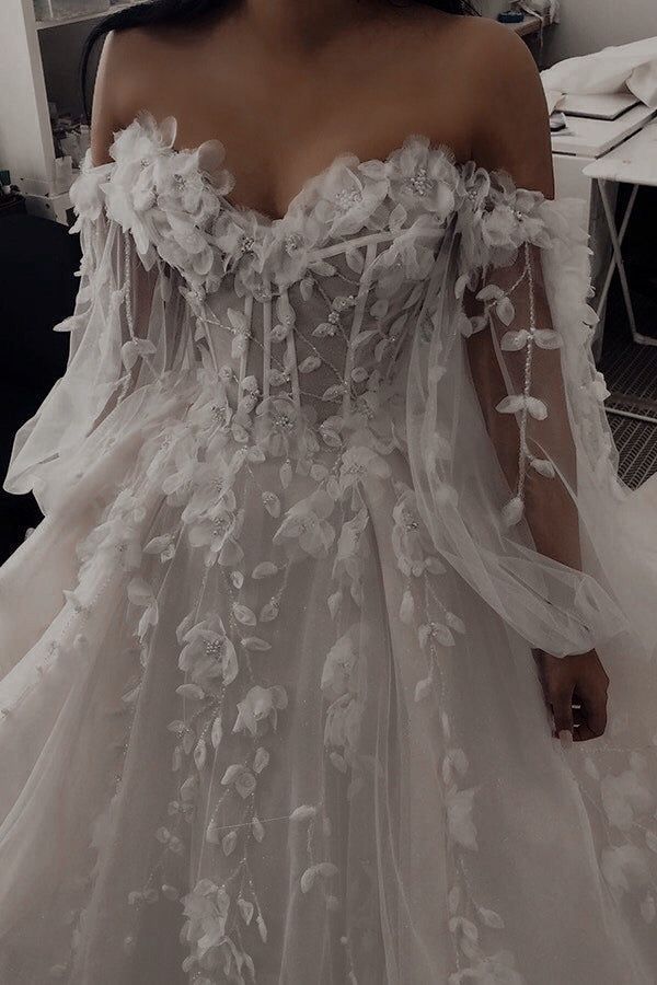 a woman wearing a white wedding dress with flowers on the skirt and off the shoulder