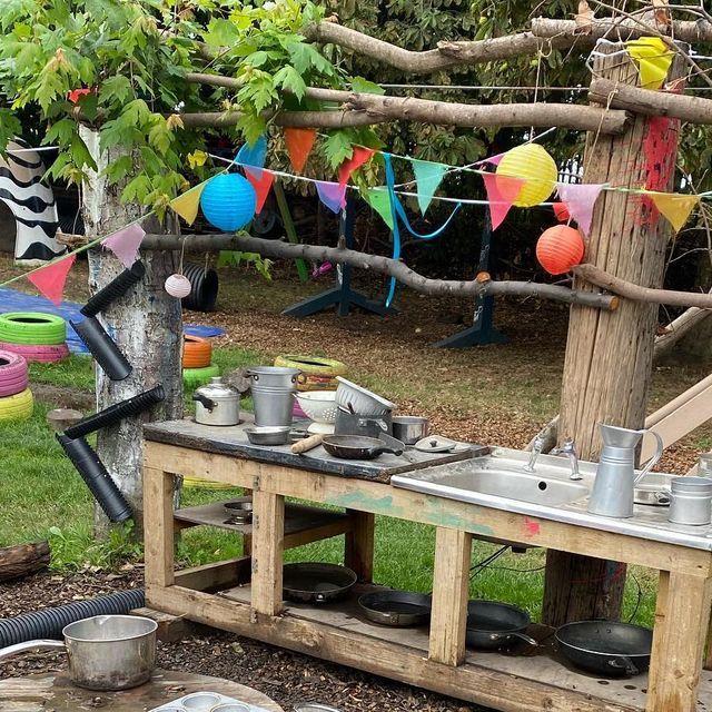 an outdoor cooking area with pots and pans on the stove, in front of a tree