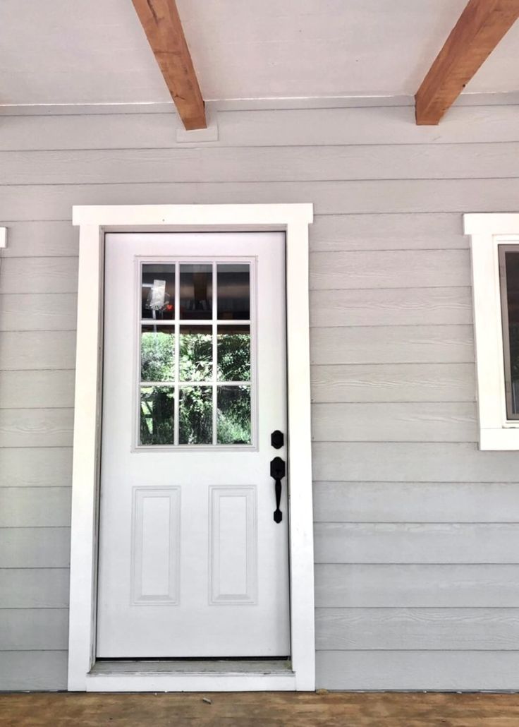 a white front door with two windows on the side of a gray house that has wood beams