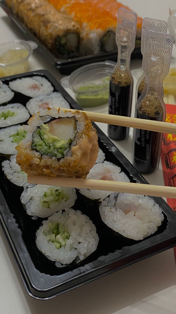 sushi and chopsticks on a black tray with condiments in the background