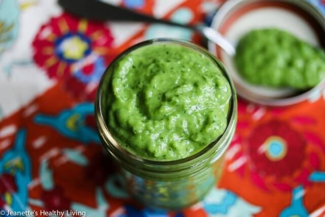 a jar filled with green sauce sitting on top of a colorful table cloth next to two small bowls