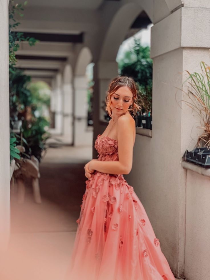 a woman in a pink dress is standing by a wall and looking at the camera