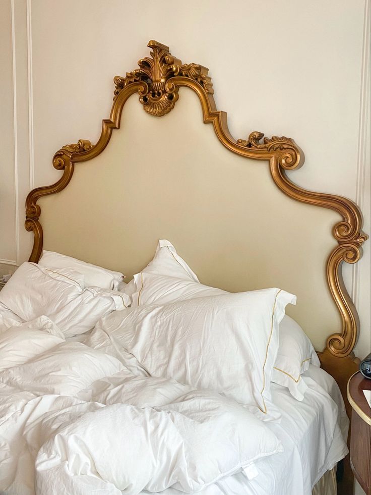 a bed with white sheets and gold headboard