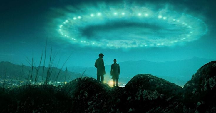 two people standing on top of a hill looking at an alien ring in the sky