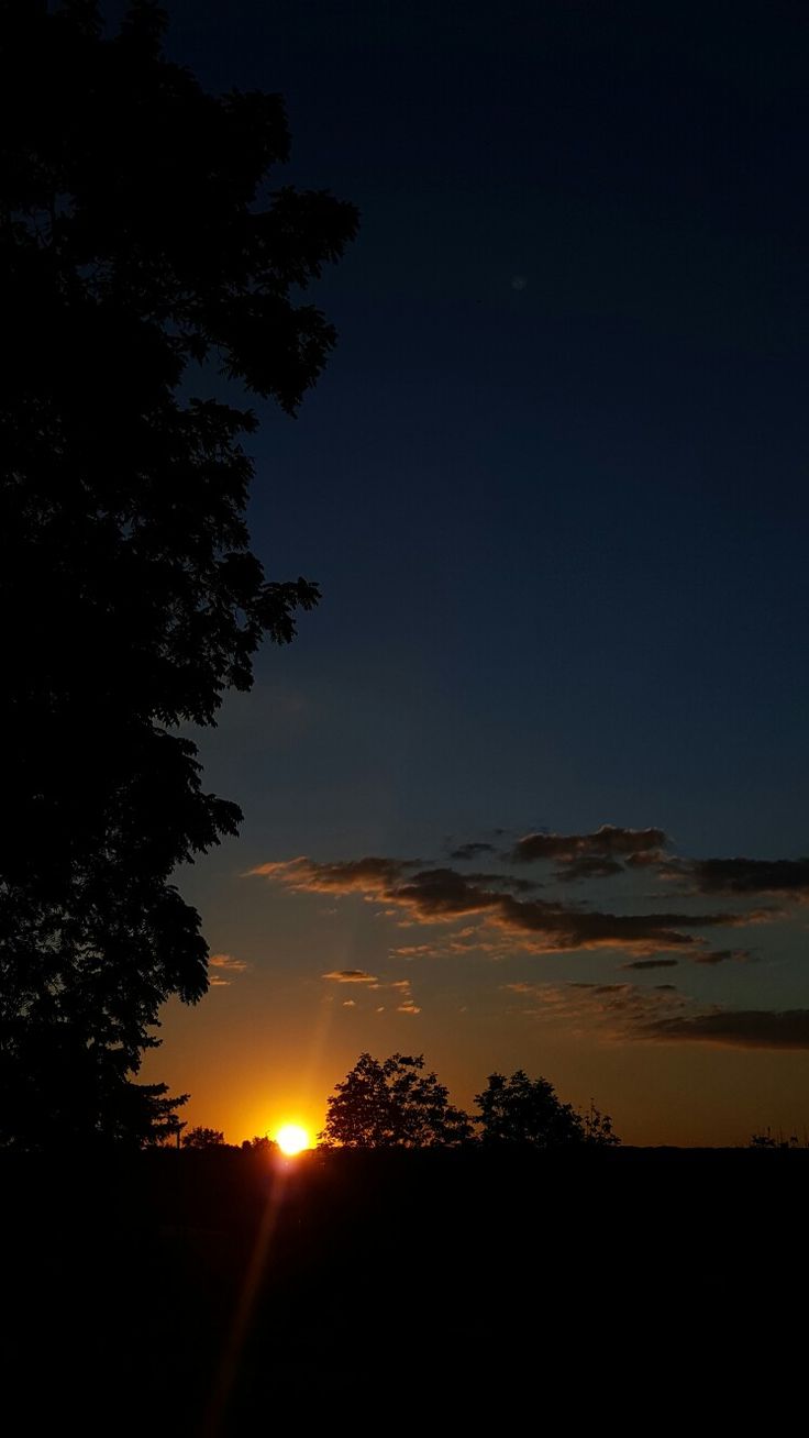 the sun is setting behind some trees in the dark sky with no one around it