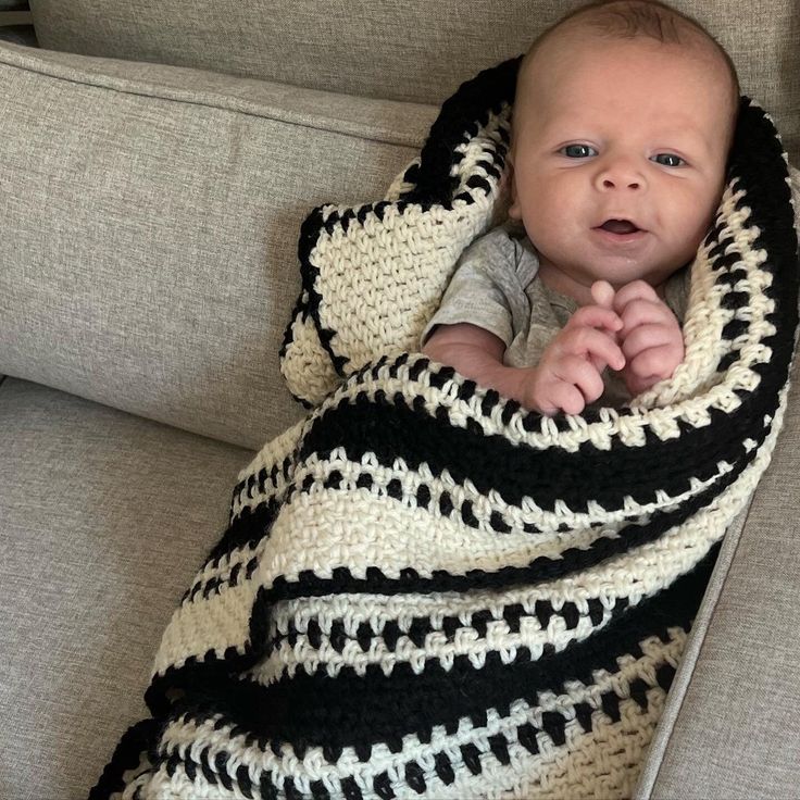 a baby wrapped in a black and white crochet blanket on top of a couch