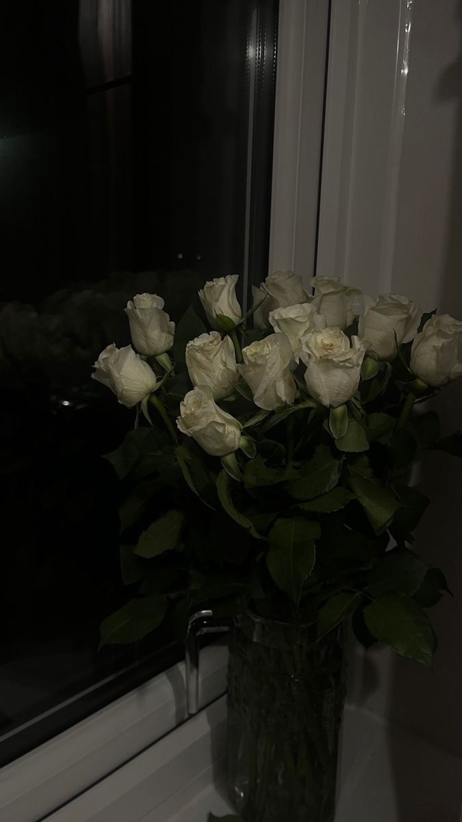 a vase filled with white roses sitting next to a window