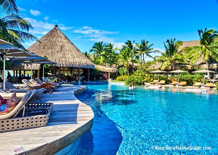 people are lounging on lounge chairs by the pool in front of thatched umbrellas