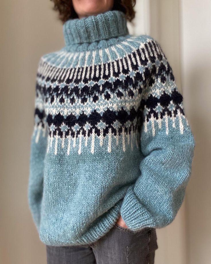 a woman wearing a blue and white sweater standing in front of a door with her hands on her hips