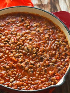 a red pot filled with beans on top of a wooden table next to an orange napkin