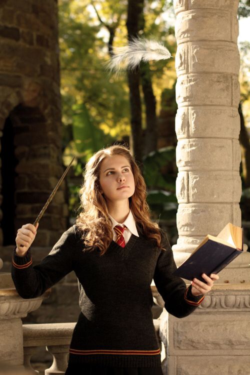 a woman in a harry potter costume holding a wand and an open book while standing next to a pillar