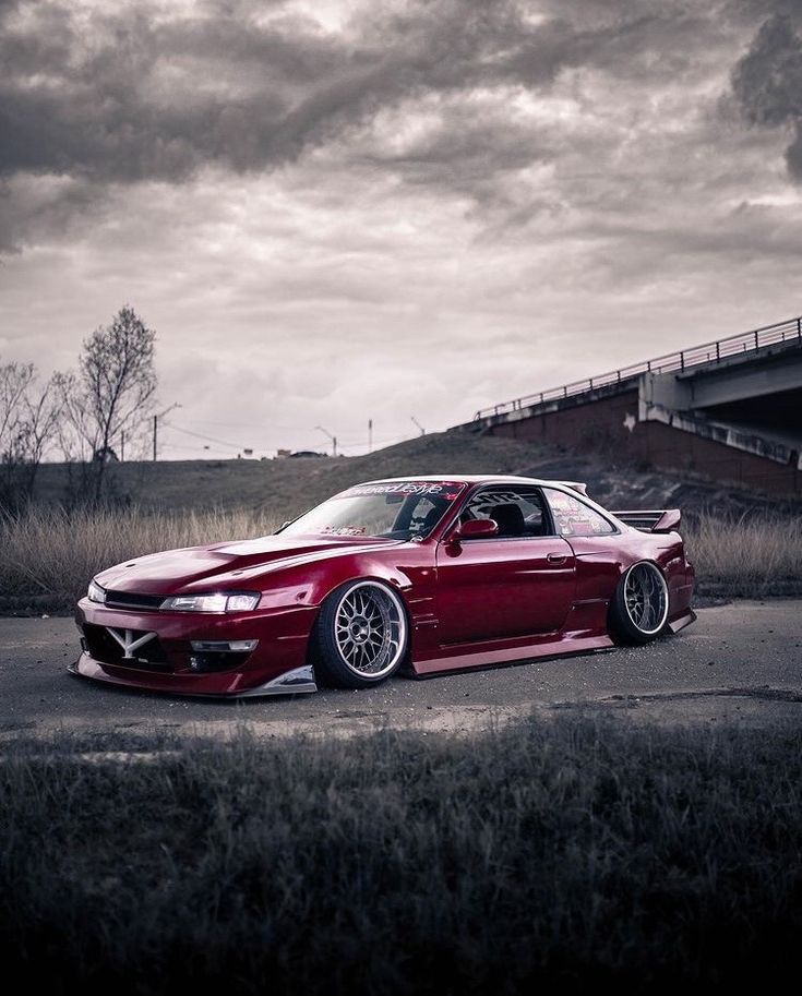 a red sports car parked in front of a bridge on a cloudy day with dark clouds