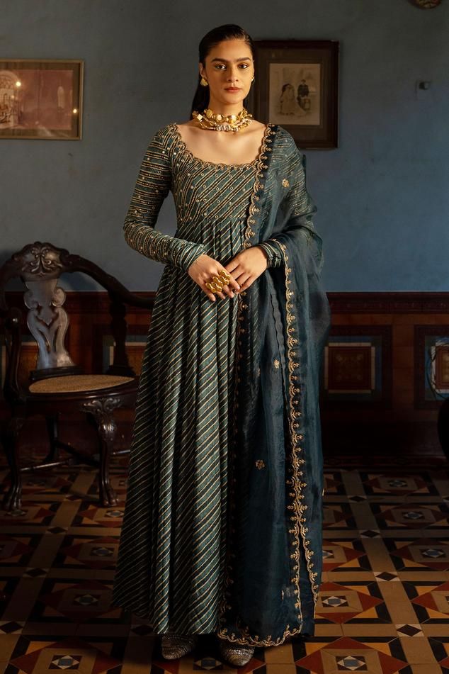 Teal cotton silk padded anarkali with leheriya print, antique gold toned resham thread, zari, mirror, beads, sequin hand work yoke and churidar sleeves. Paired with tissue dupatta with all over hand work.
Components: 2
Pattern: Printed and Hand Embellished
Type Of Work: Leheriya Print, Resham Thread, Mirror, Zari, Beads and Sequin Work
Neckline: Round Neck
Sleeve Type: Churidar Sleeves
Fabric: Anarkali: Cotton Silk, Dupatta: Tissue
Color: Blue,Green
Other Details: 
Karigari time: 69 hrs
Scallope Navy Blue Anarkali, Paulmi And Harsh, Blue Anarkali, Printed Anarkali, Designer Anarkali Suits, 1950’s Fashion, Embroidered Anarkali, Designer Anarkali, Simple Pakistani Dresses