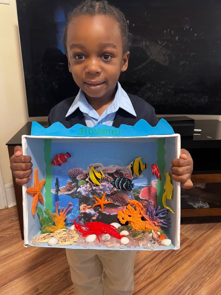 a young boy holding up a box with fish in it and an aquarium inside the box