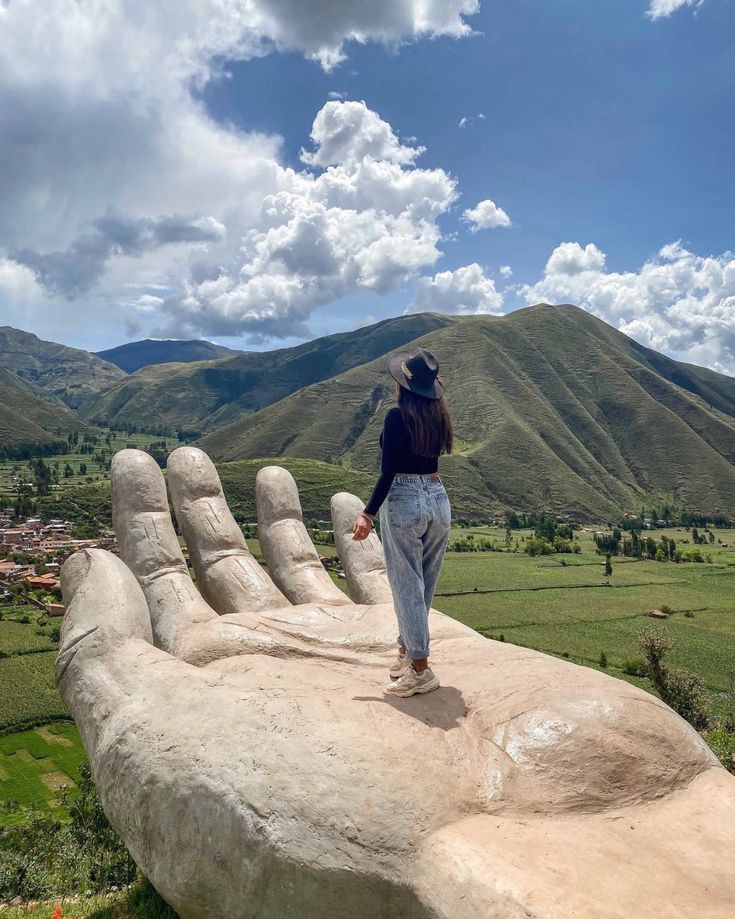 a person standing on top of a giant hand statue in the middle of a field