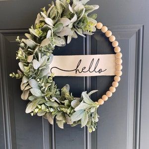 a wreath with the word hello on it hanging on a front door, next to a sign that says hello