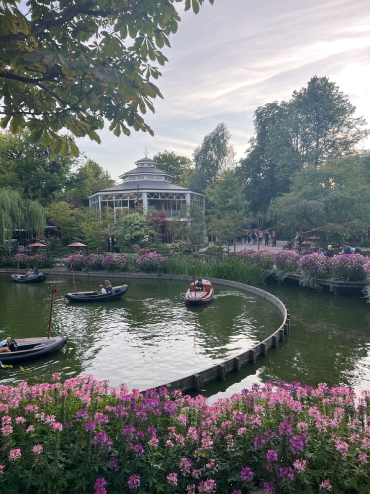 several boats floating on top of a lake surrounded by flowers and greenery in front of a gazebo