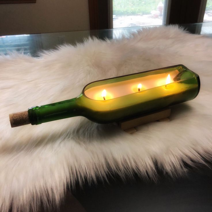 a bottle with some candles in it on a fur covered table next to a window