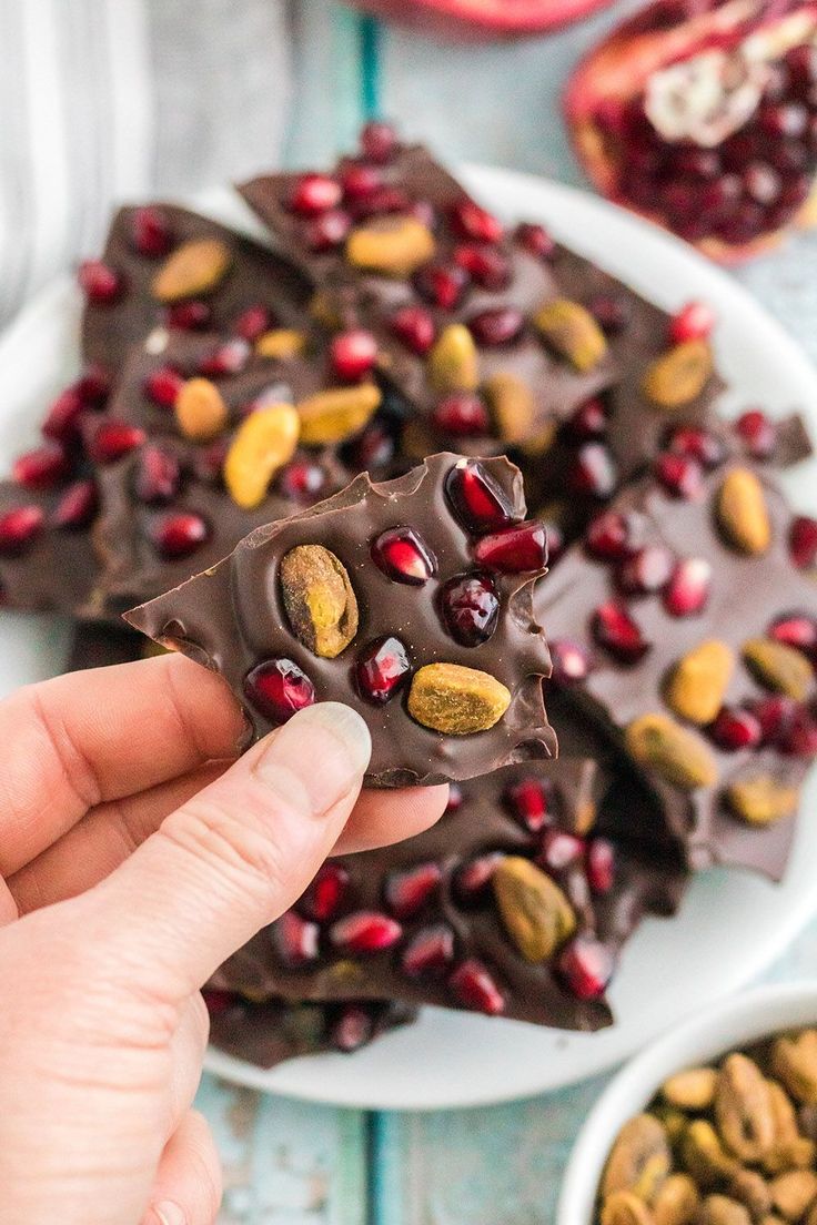 a hand holding a piece of chocolate bark with nuts and pomegranates