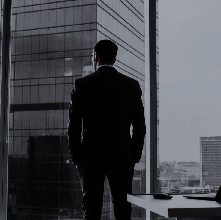 a man standing in front of a window looking out at a cityscape with skyscrapers