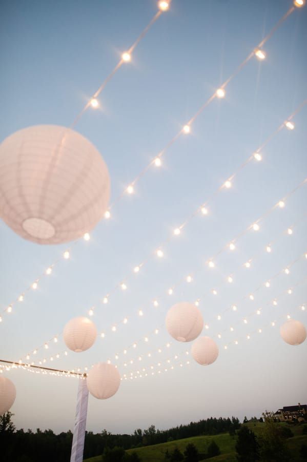 white paper lanterns hanging from the ceiling and string lights strung over it at night time