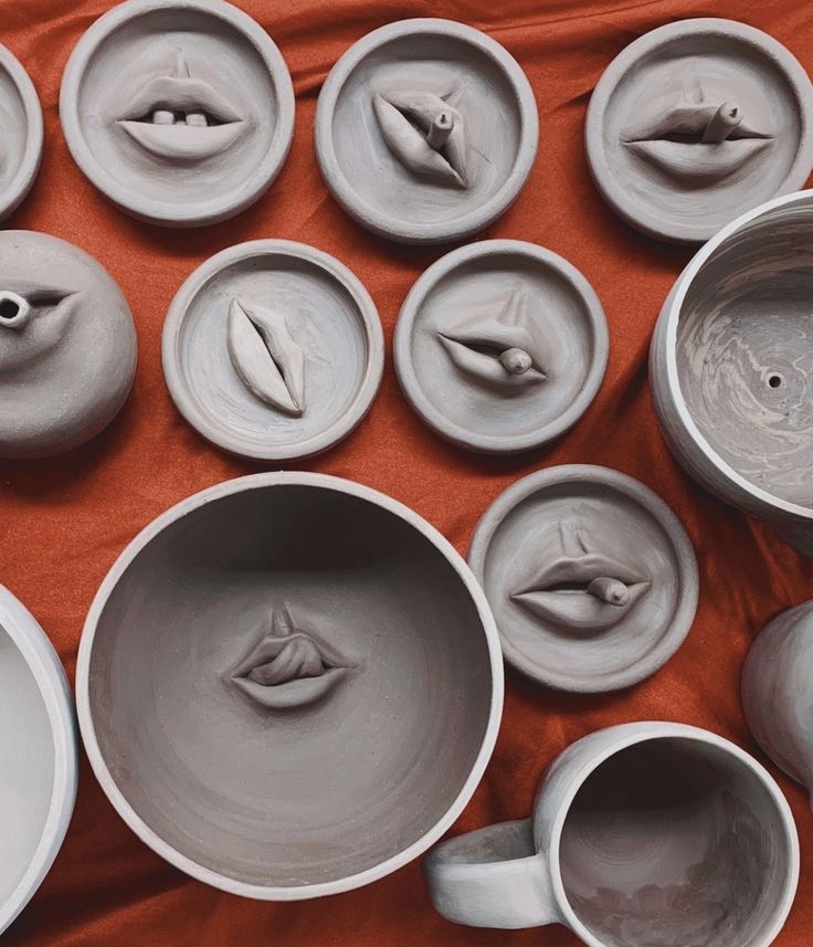 several bowls and cups are arranged on a red table cloth, with one being made to look like the mouth of a bird