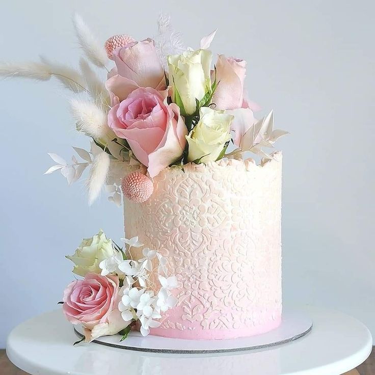 a pink and white wedding cake with flowers on the top is sitting on a table