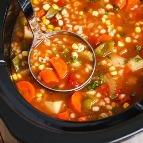 a spoon full of soup with carrots, corn and celery in the slow cooker