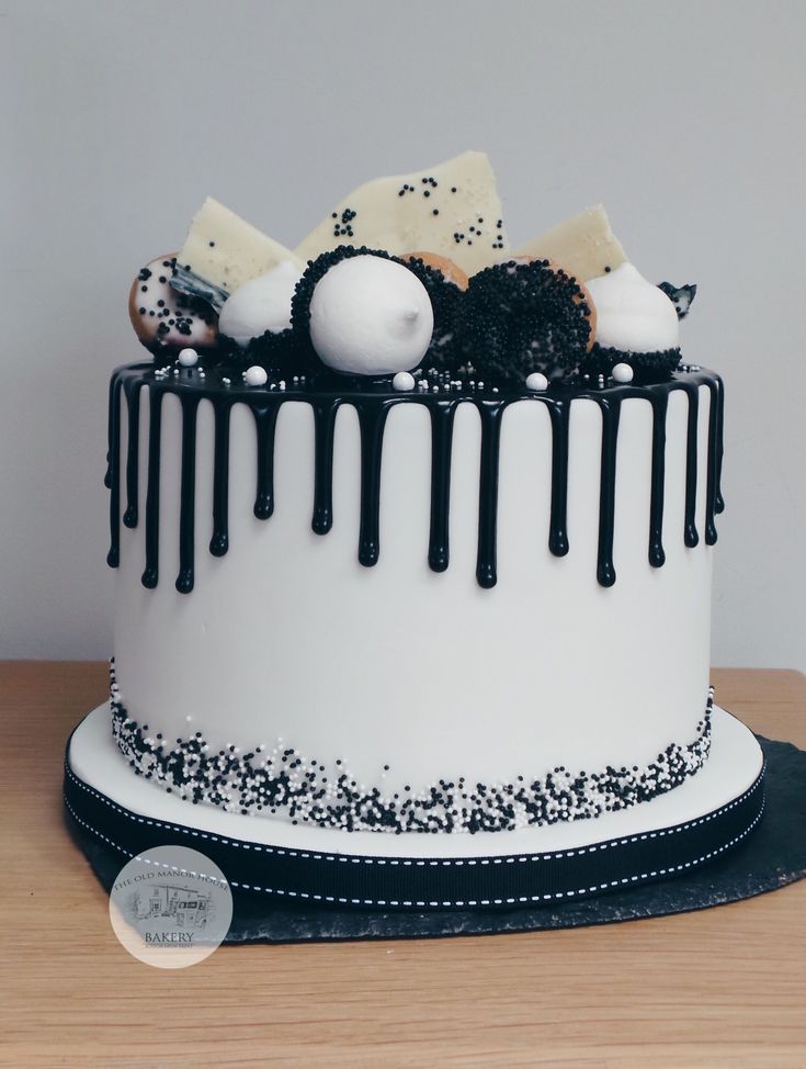 a white cake with black icing and sprinkles on the top is sitting on a wooden table