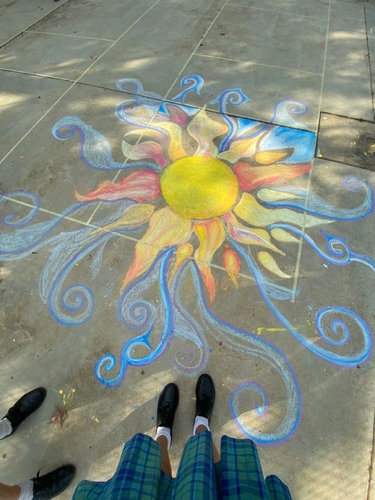 a person standing in front of a sidewalk with chalk drawings on it and the sun