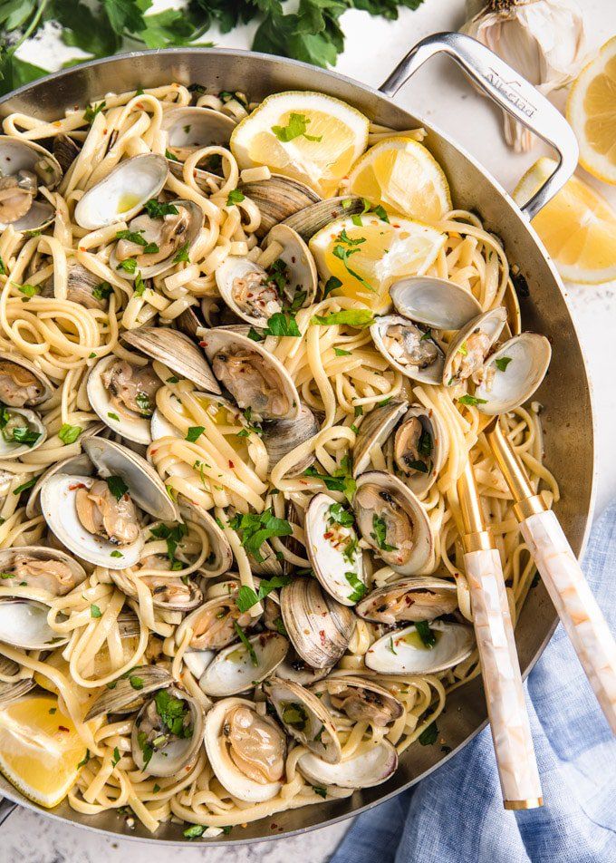 pasta with clams and parsley in a skillet next to lemon wedges