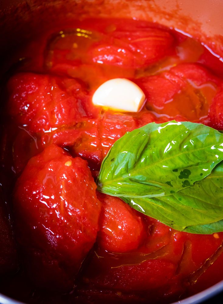 tomatoes and basil cooking in a pot with red liquid on the bottom, ready to be cooked