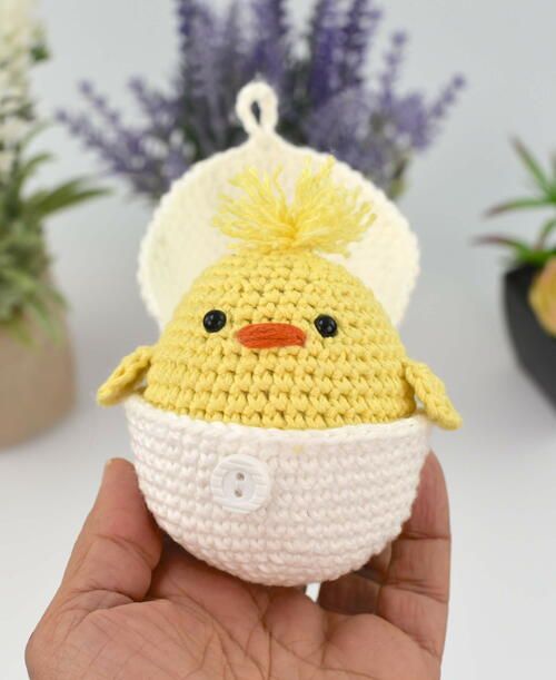 a hand holding a small yellow and white crocheted chick